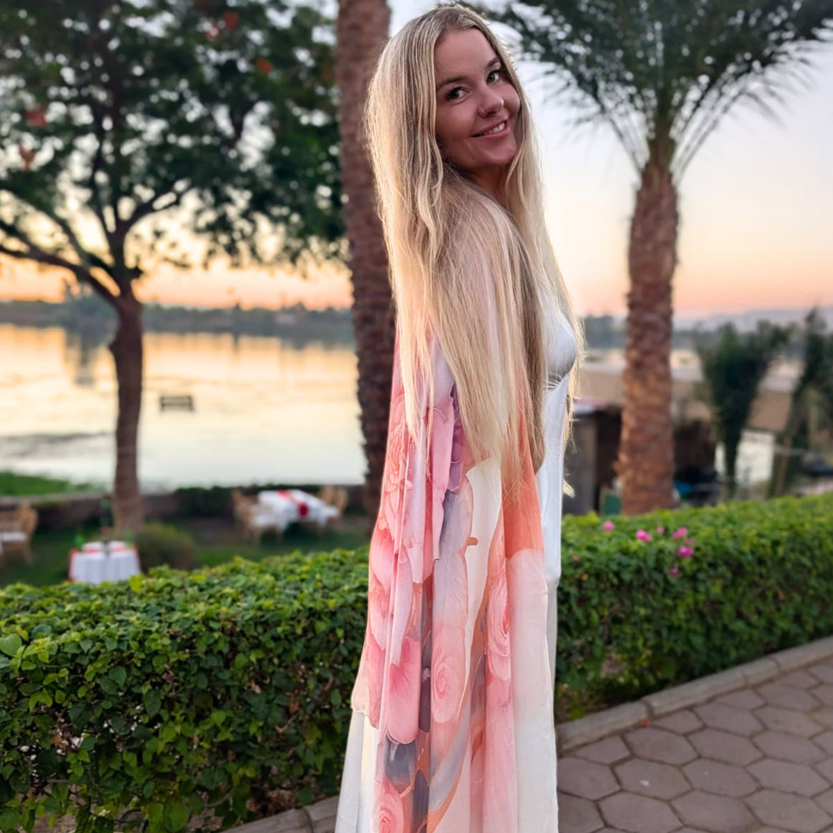 Woman wearing the pink rose Bliss Shawl as a kimono wrap in a garden by the river at sunset - vegan silk festival shawl