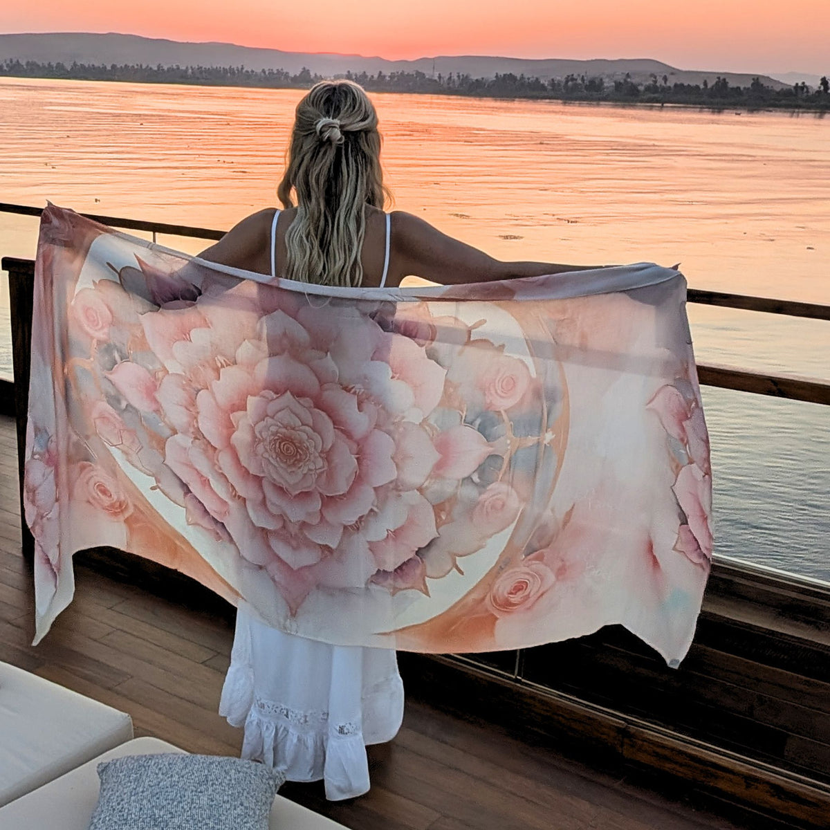Woman holding the Bliss Shawl open at sunset over the water, pink rose mandala vegan silk spiritual scarf