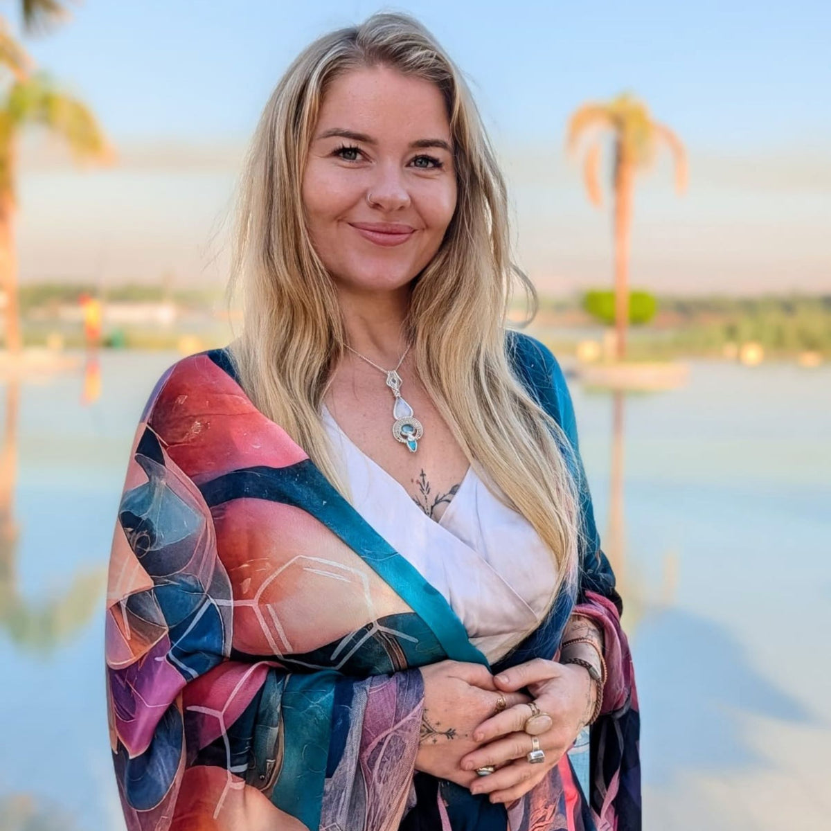 Woman smiling at the lake wrapped in the Calm Shawl, blue and coral lotus vegan silk meditation scarf