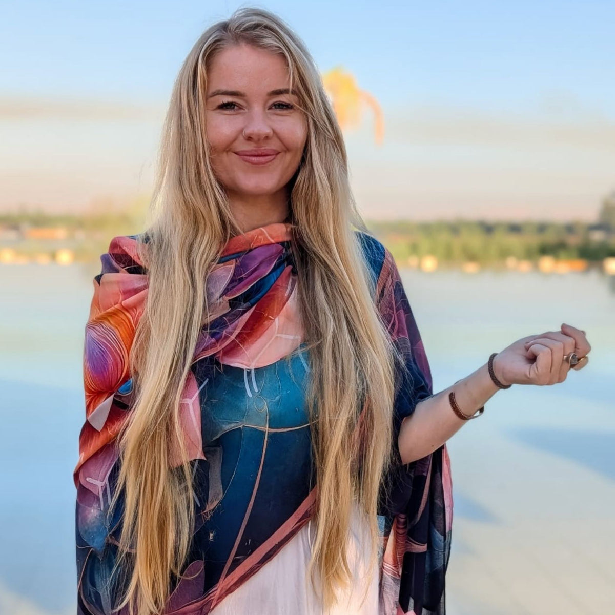Smiling woman by the water wearing the colourful Calm Shawl draped over her shoulders - lotus meditation wrap