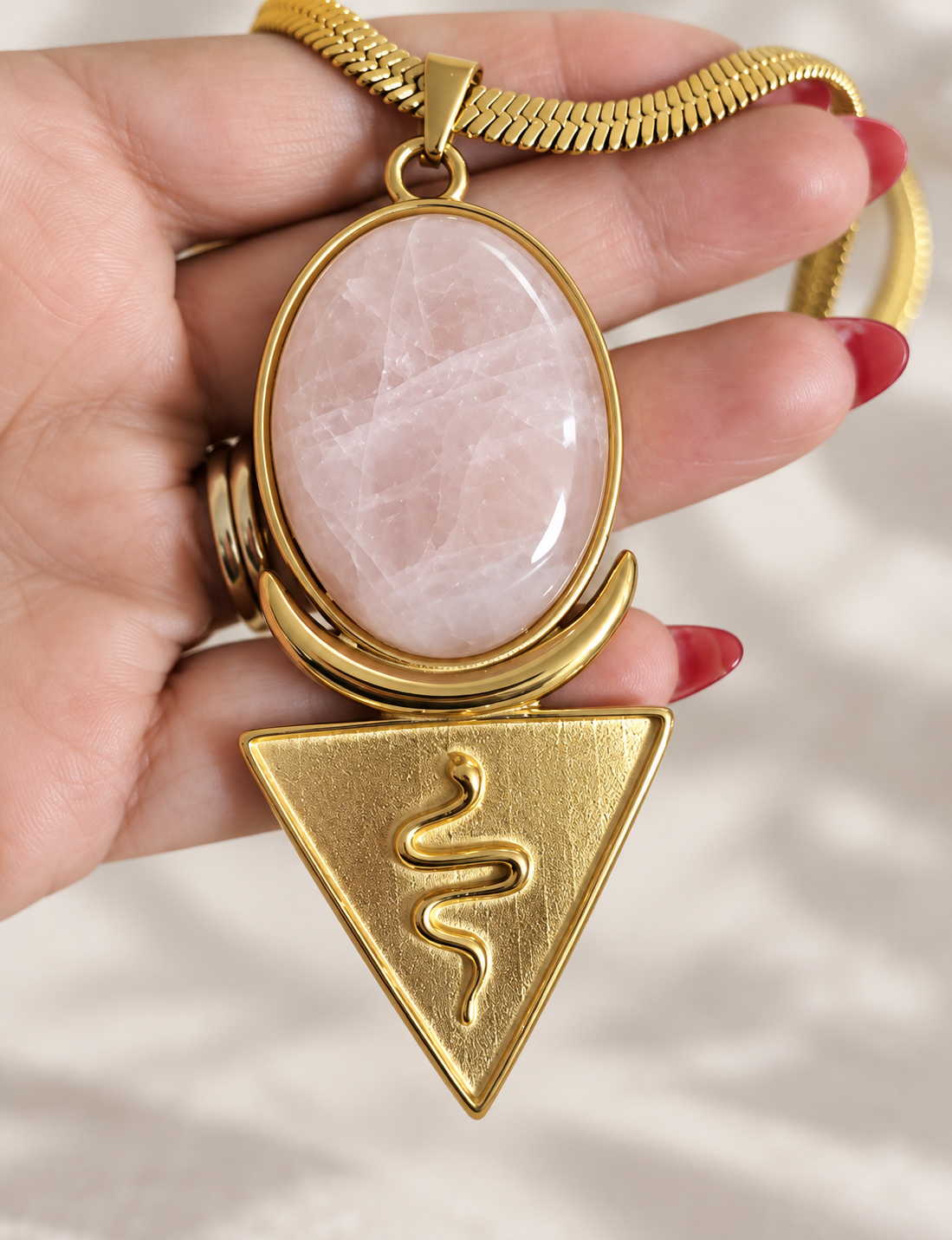 Rose quartz priestess necklace held in hand, oval rose quartz gemstone above a gold serpent triangle