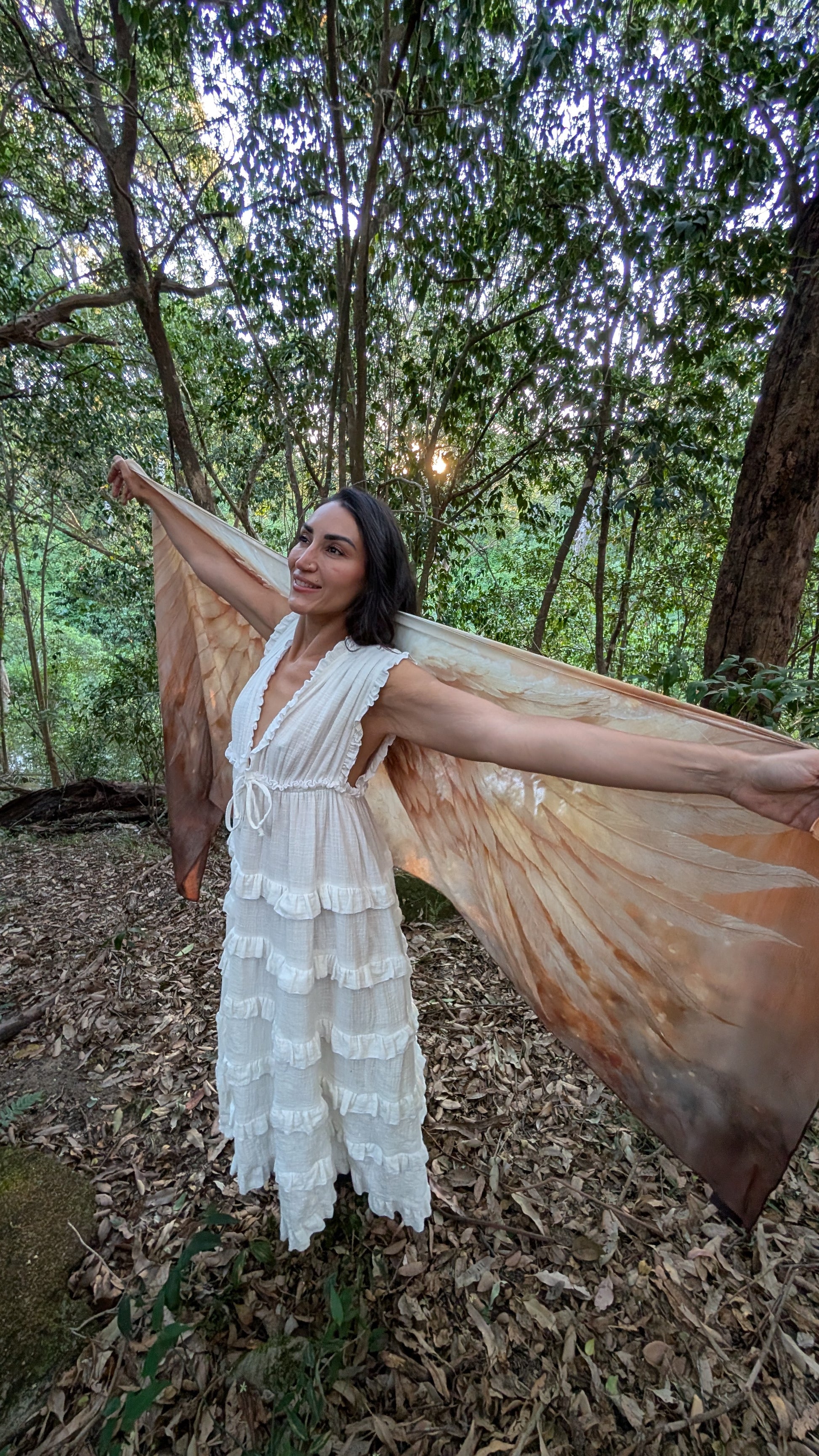 Woman wearing the Abundance Shawl as festival wear, an oversized natural fibre scarf with gold wing artwork for boho festival fashion