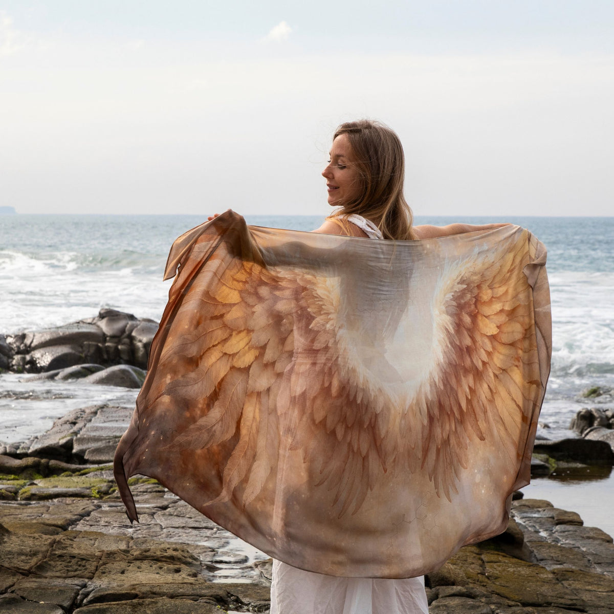 Woman on ocean rocks spreading the gold angel wing Abundance Shawl like wings - spiritual festival shawl
