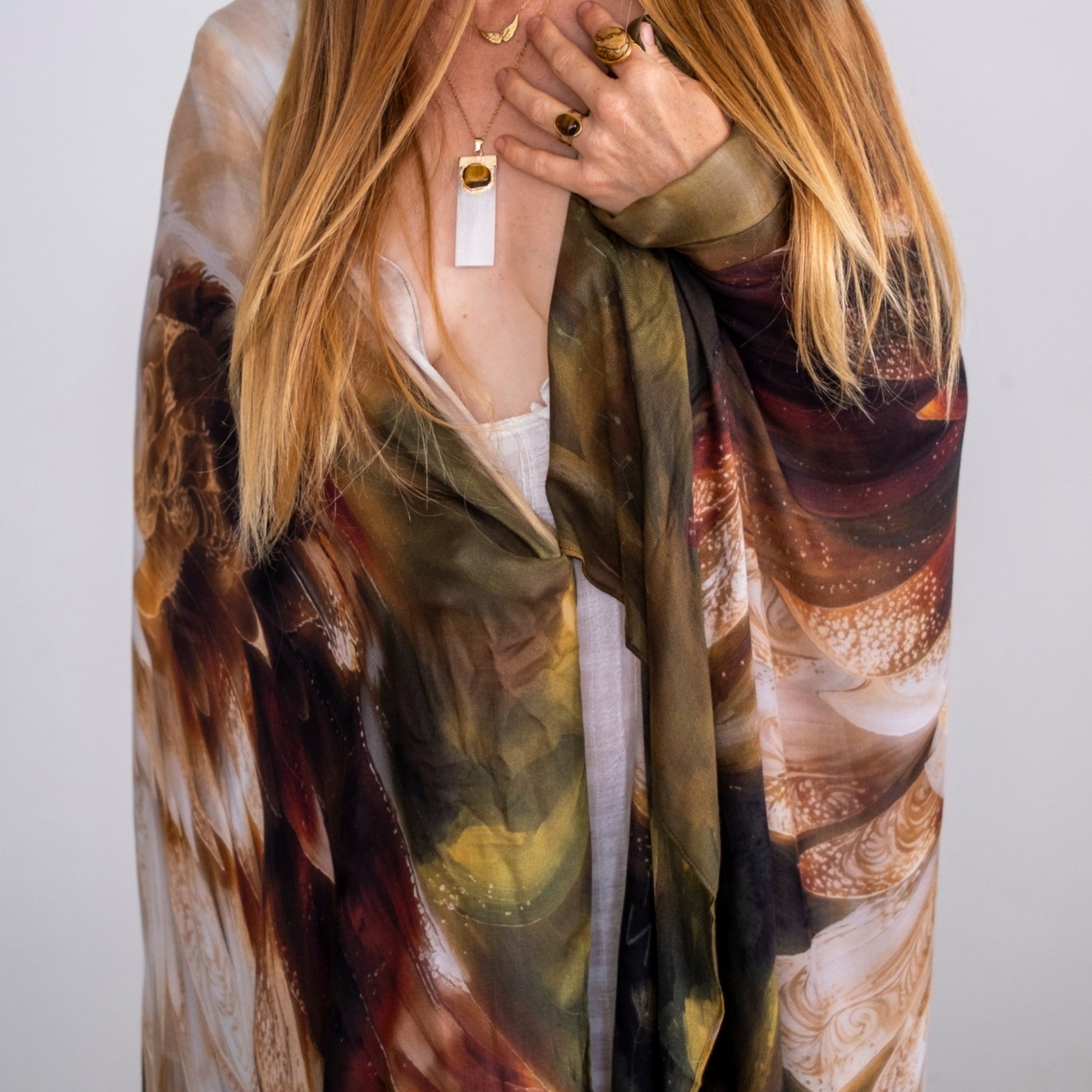Woman wearing the Grounded Presence Shawl featuring angel wings and white lotus artwork in a flowing wearable wellness design