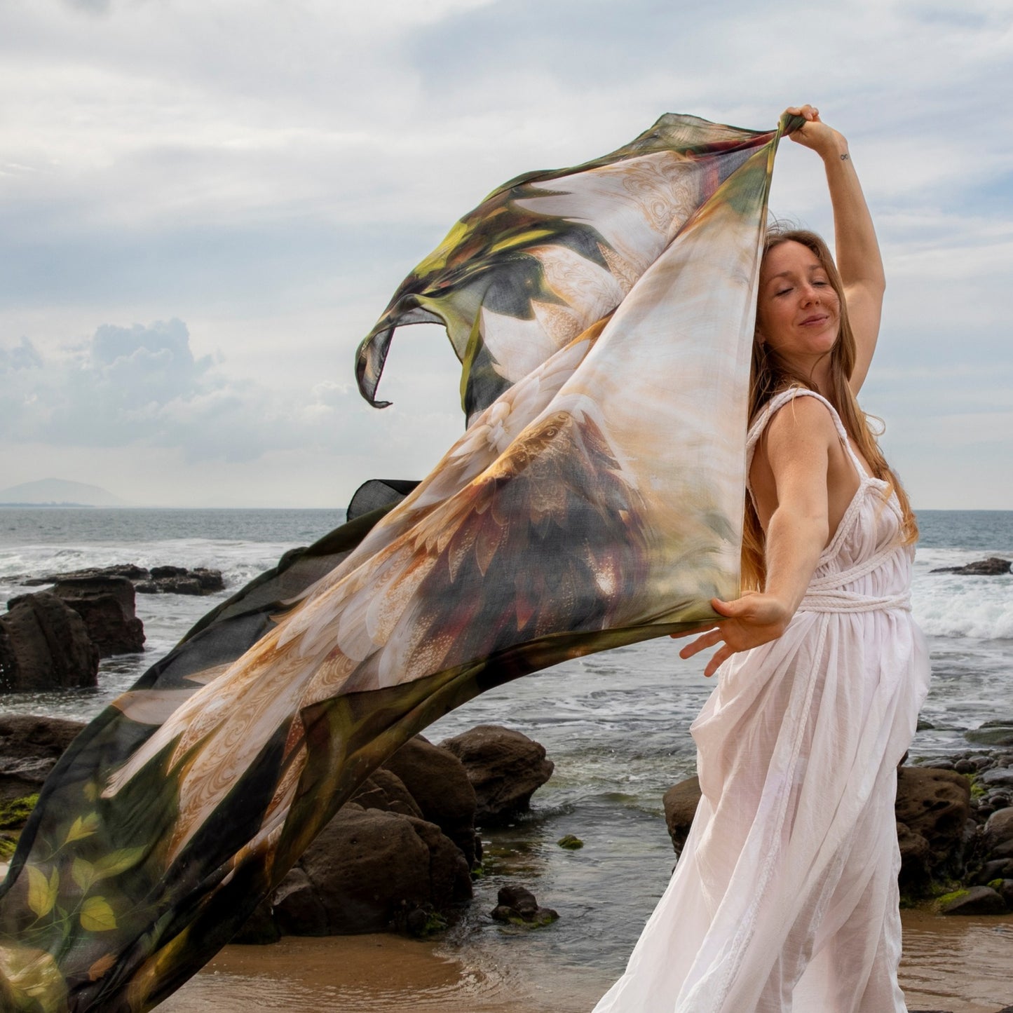 Grounded Presence Shawl by Original Molecule Shawls featuring angel wings and white lotus artwork worn beside the ocean