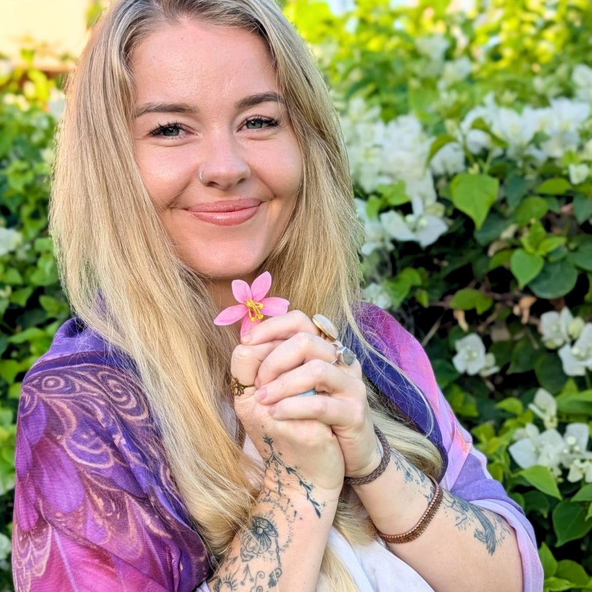 Smiling woman holding a pink flower while wearing the Happiness Shawl purple angel wing wrap