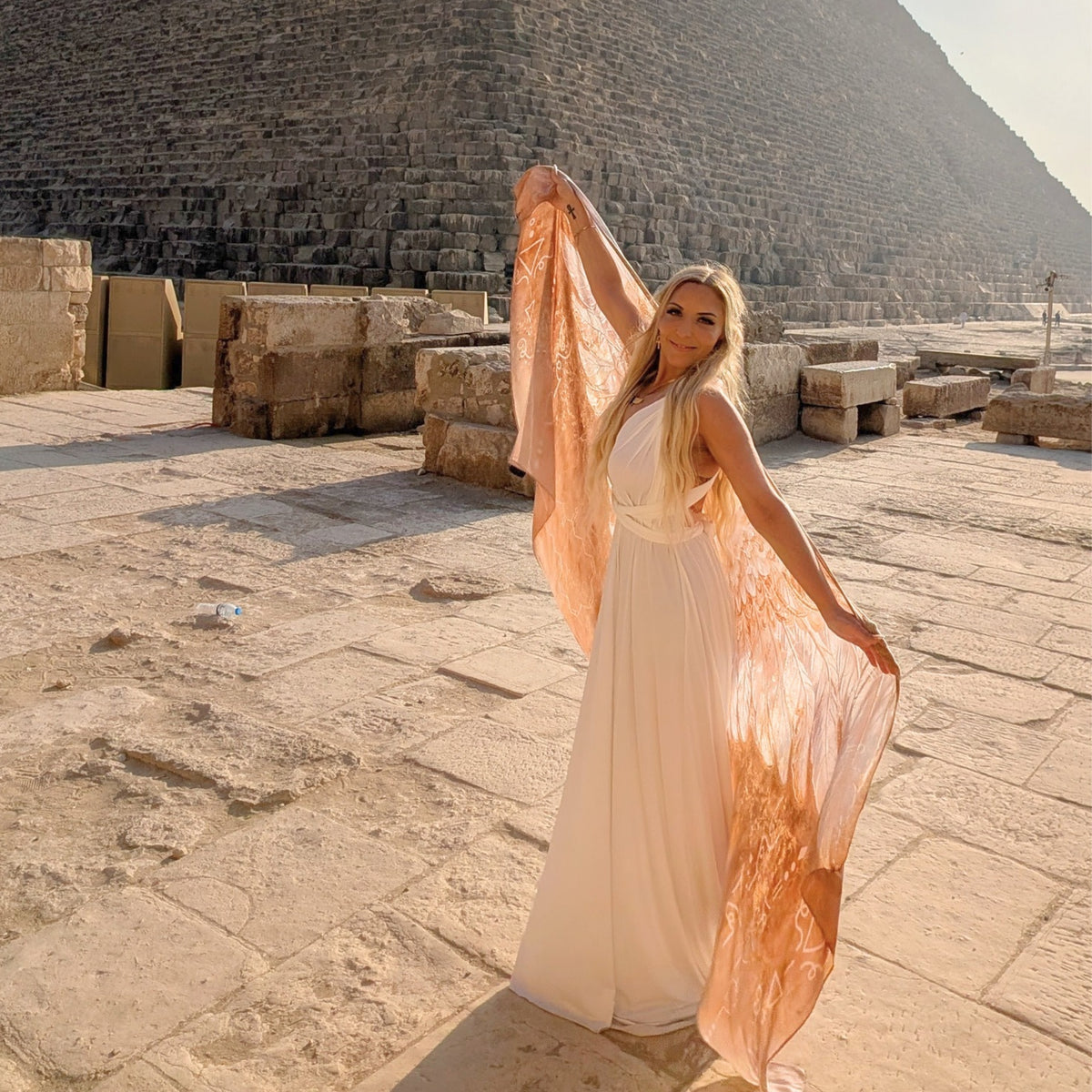 Woman in a white dress holding the Safety Shawl gold and white angel wings at an Egyptian pyramid