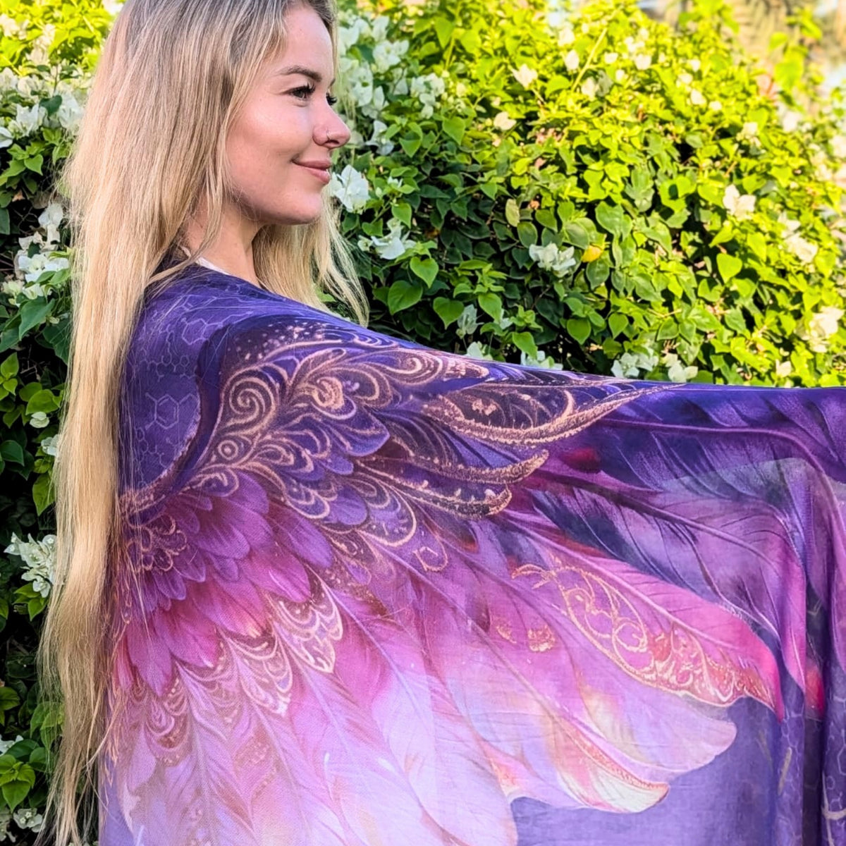 Happiness Shawl purple and pink angel wings with gold detail held open in a lush garden