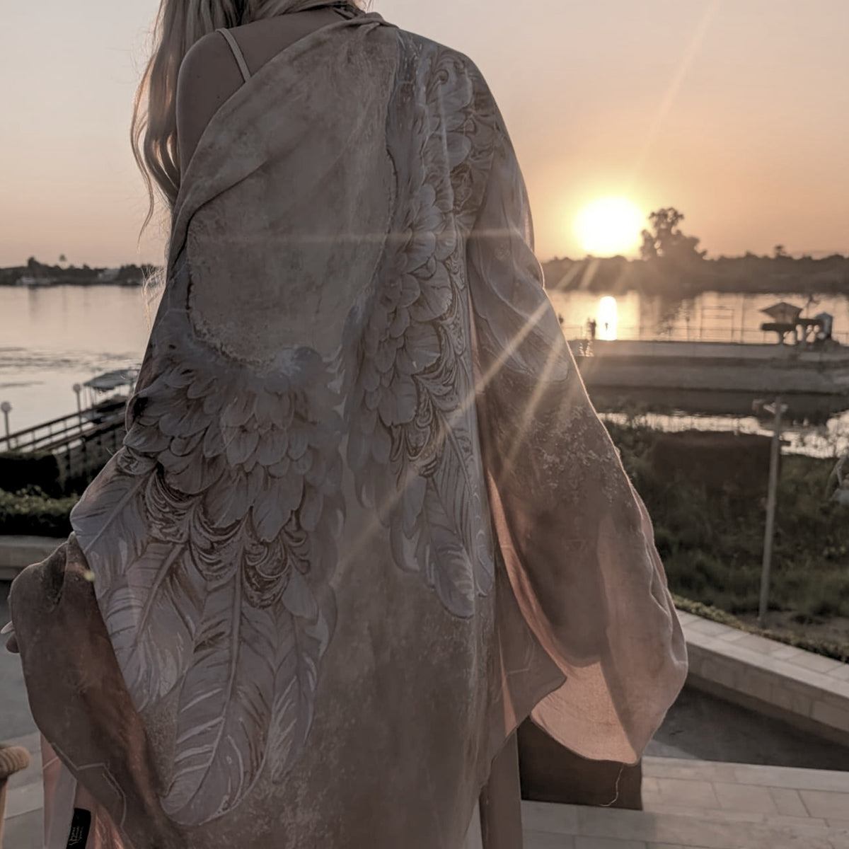 Back view of the Safety Shawl gold and white angel wing wrap at sunset over the water